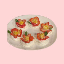 Mini pavlova cakes topped with kiwi and strawberry arranged in floral patterns, served on a white plate for events or parties